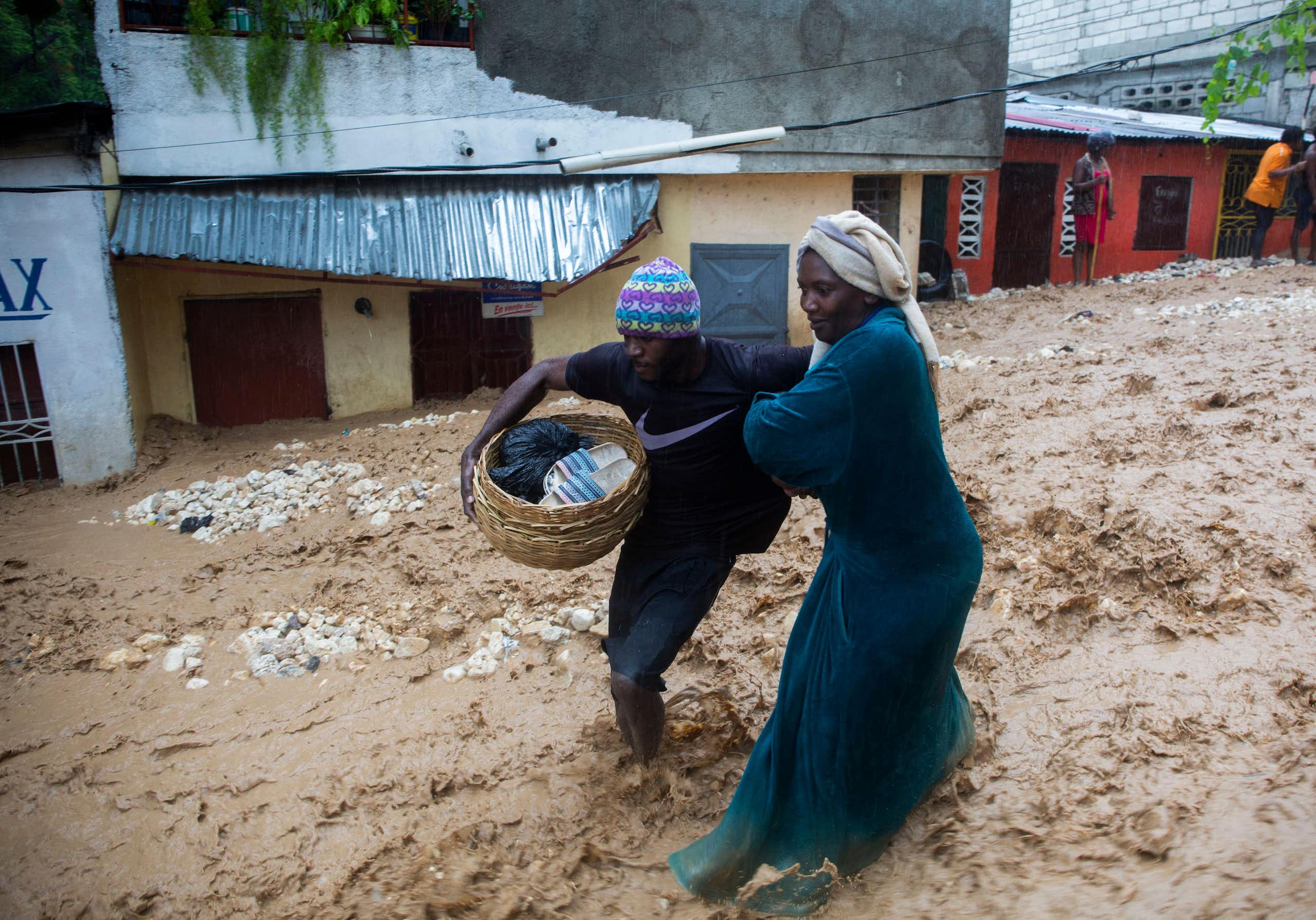 Two women struggle through a street flooding with muddy water in Haiti. One carries a basket