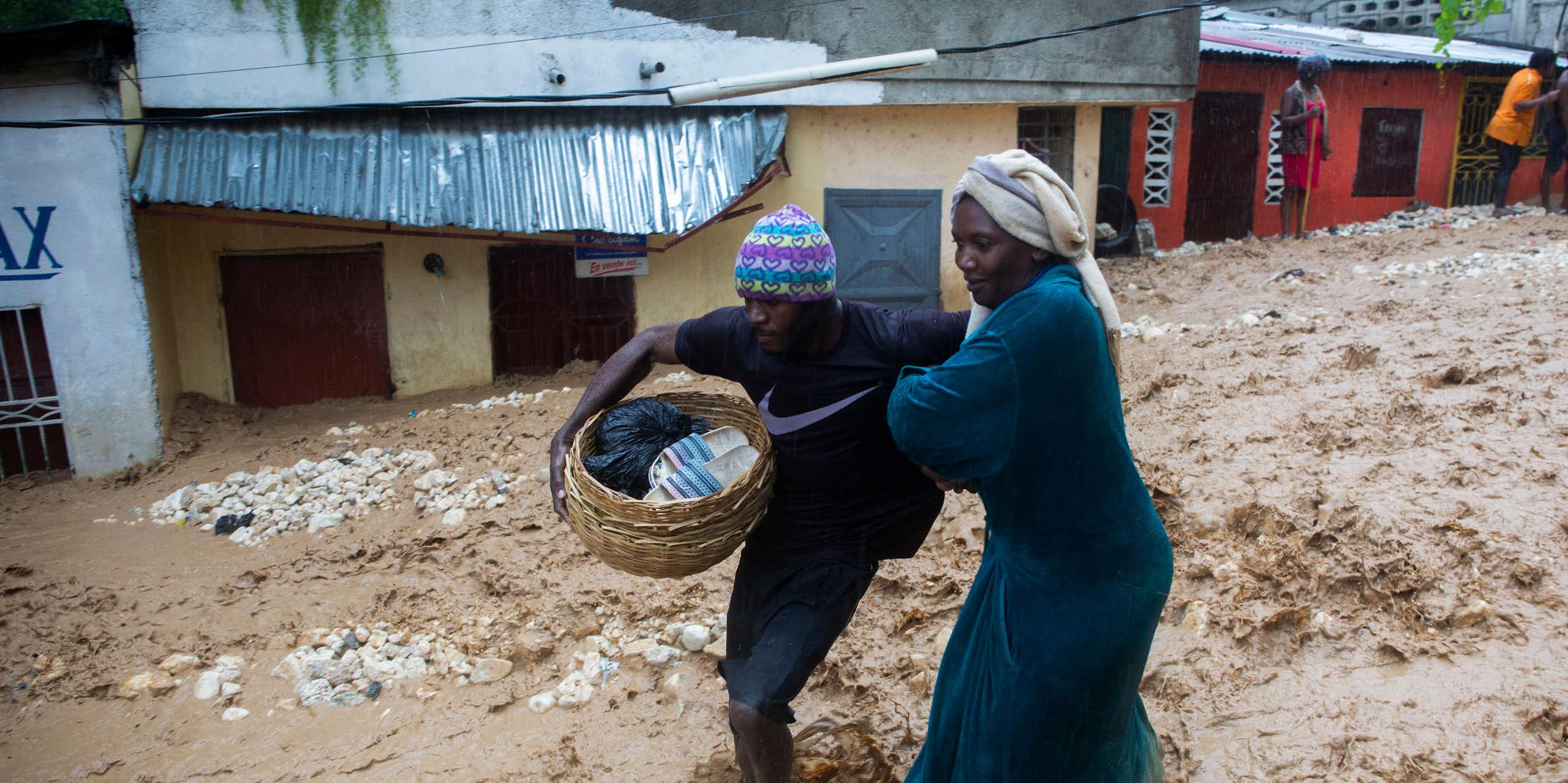 Two women struggle through a street flooding with muddy water in Haiti. One carries a basket