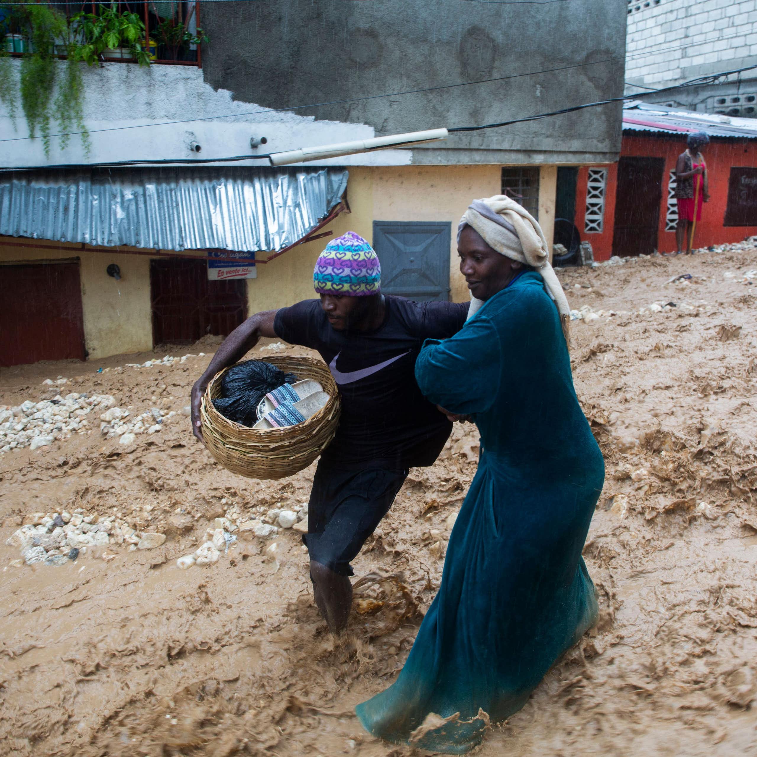 Two women struggle through a street flooding with muddy water in Haiti. One carries a basket