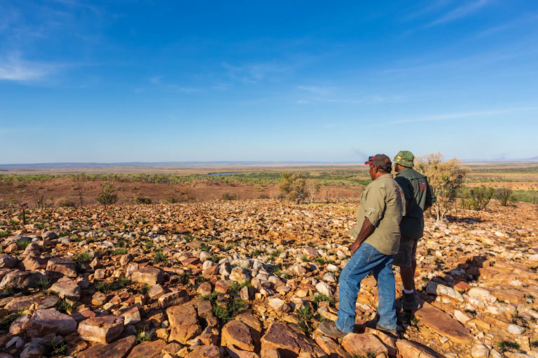 Two Indigenous men look out across an Australian landscape.