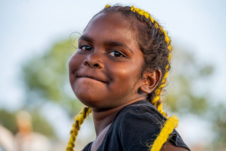 A young Aboriginal girl smiles at the camera.