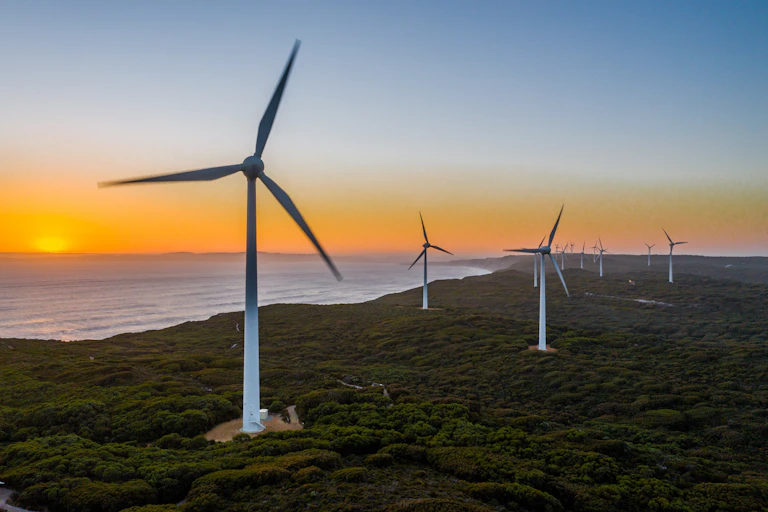 A wind farm is set against a golden sky near the ocean in Australia.
