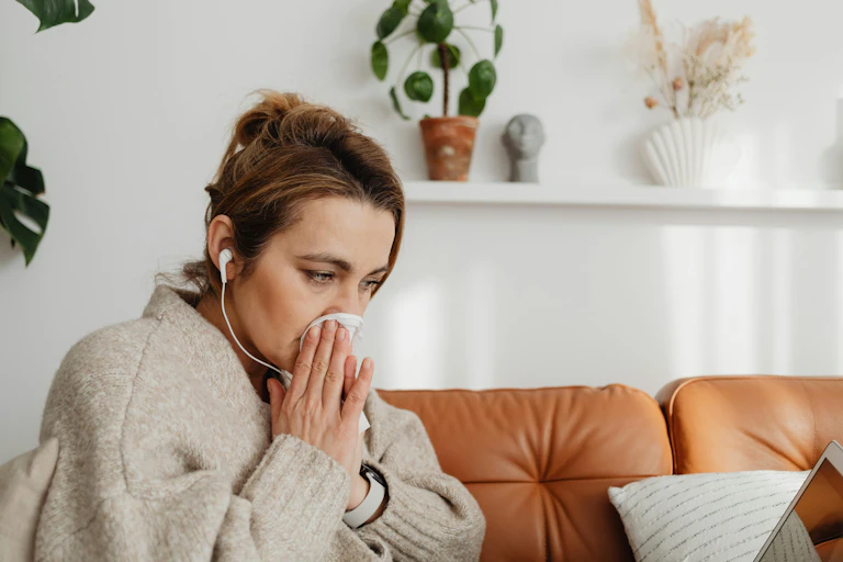 Woman blows her nose while sitting on a couch