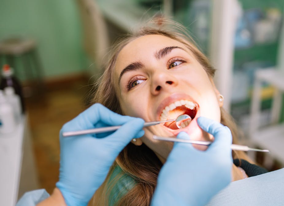 A young woman looks at her dentist who is using instruments to probe her teeth.
