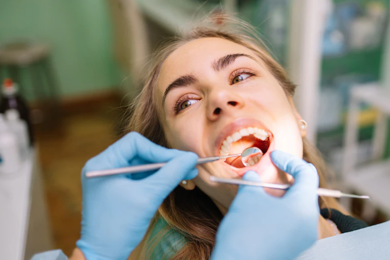 A young woman looks at her dentist who is using instruments to probe her teeth.