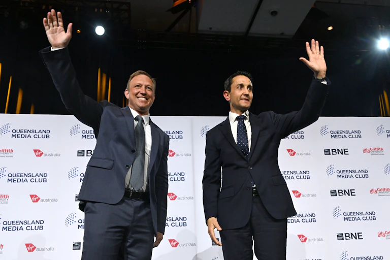 Two men in suits stand and wave at an audience