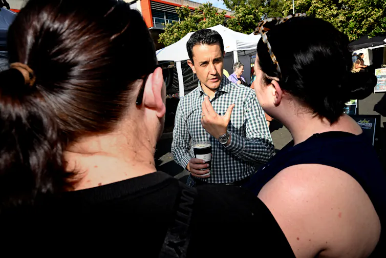 The backs of two women's heads while a man speaks to them