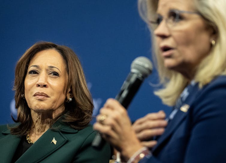 Two seated women, one with brown hair and the other with blond hair and holding a microphone.