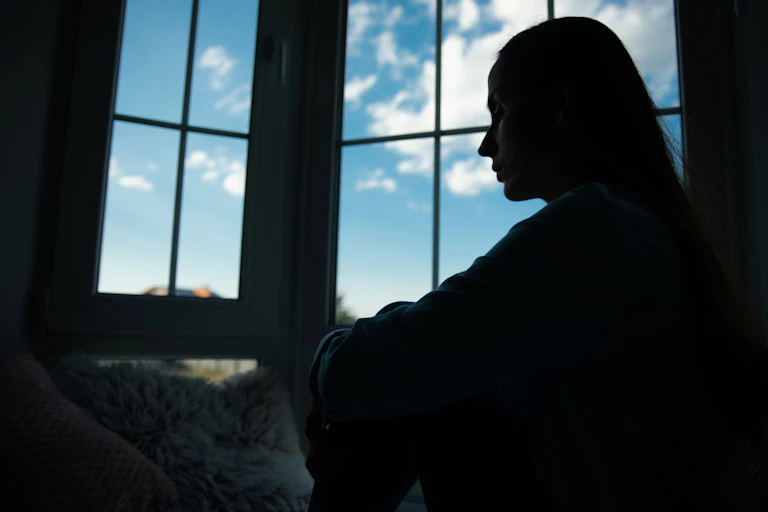 Shadowed silhouette of a woman sitting on windowsill