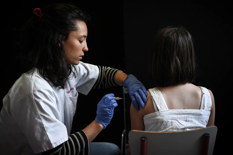 Une soignante vaccine une élève qui est de dos.