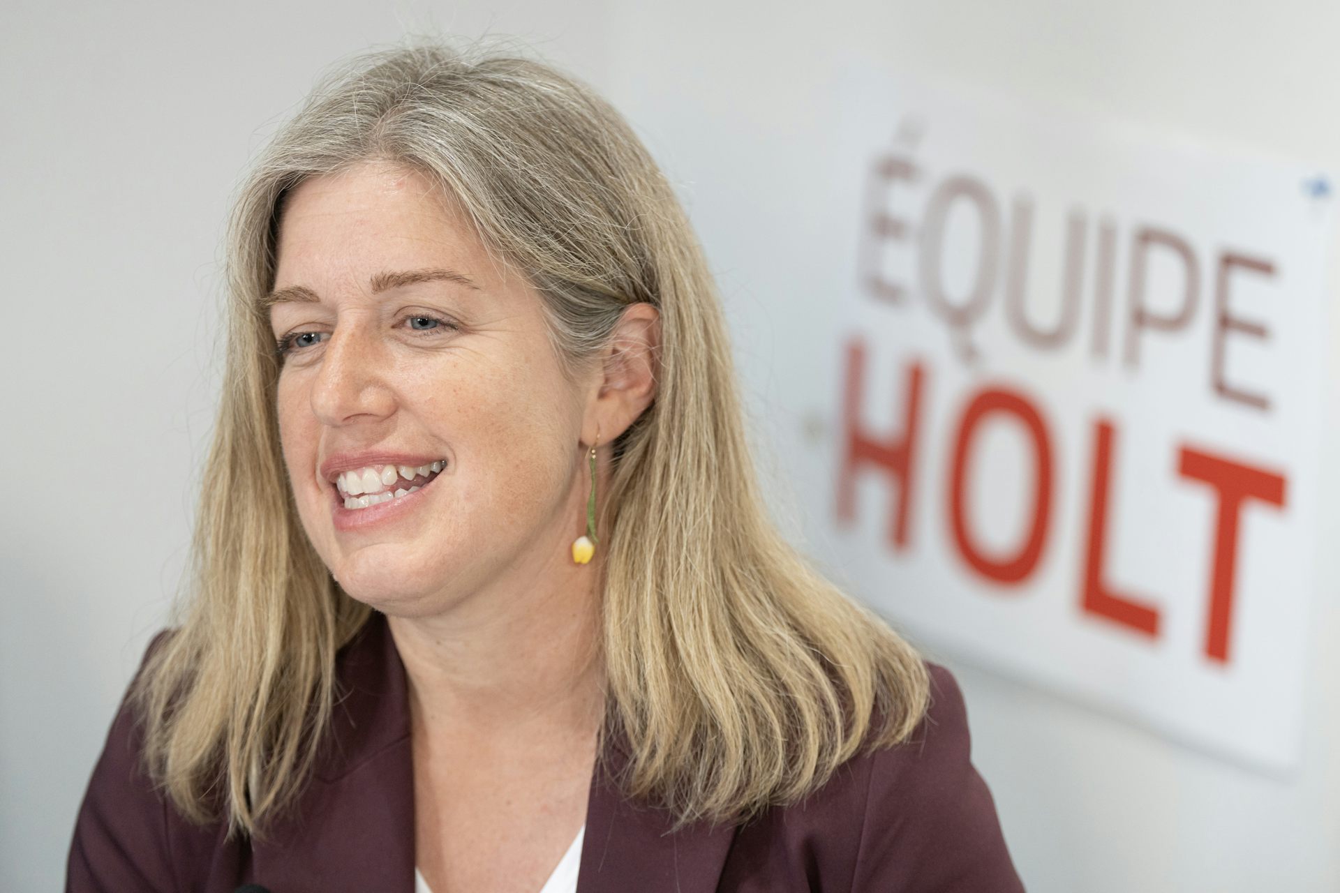 A blonde woman smiles as she sits in front of a sign that reads Equipe Holt.