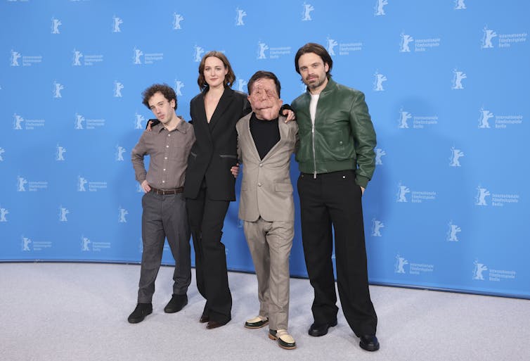 Four people posing at a premiere against a blue background.