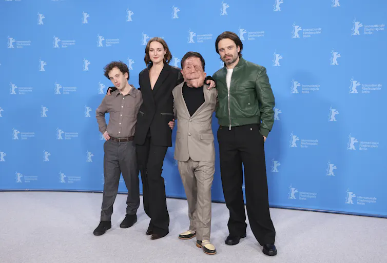 Four people posing at a premiere against a blue background.