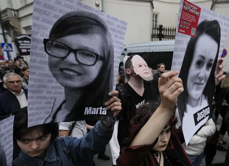 Women in black shirts hold up photos of women