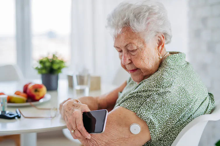 An elderly woman with a continuous glucose monitor patch looks at her phone.