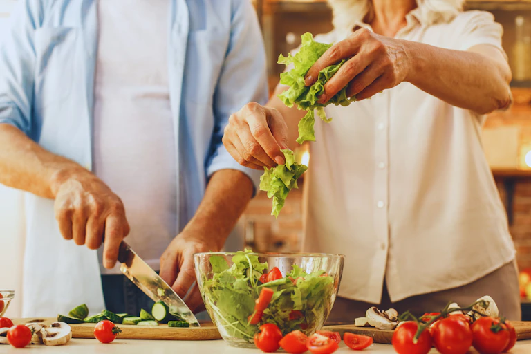 An older woman and man cut vegetables for a salad bowl.