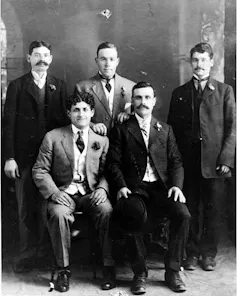 Two rows of men, the first row seated, posing for a black and white portrait while wearing suits.