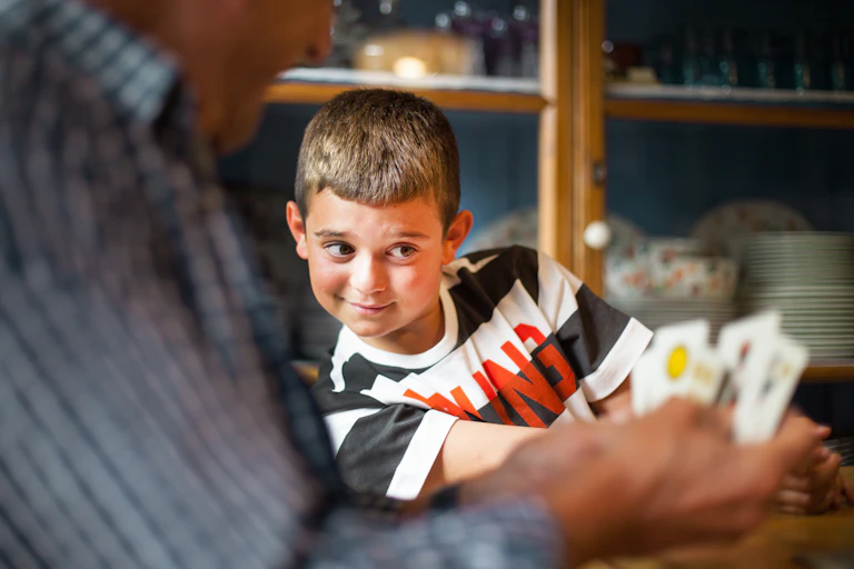 A young boy tries to peek at the cards of the adult sitting next to him.
