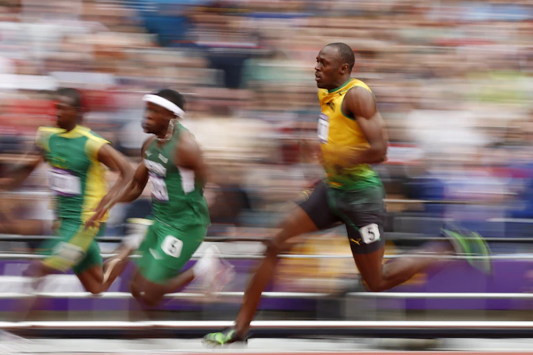 Three Olympic sprinters running on track against blurred background.