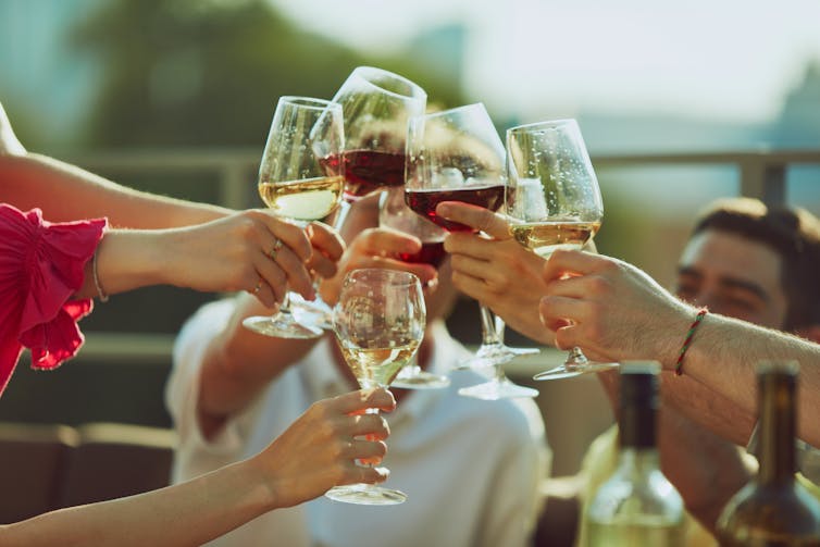 Muitas mãos batendo em taças de vinho cheias em uma noite ensolarada.