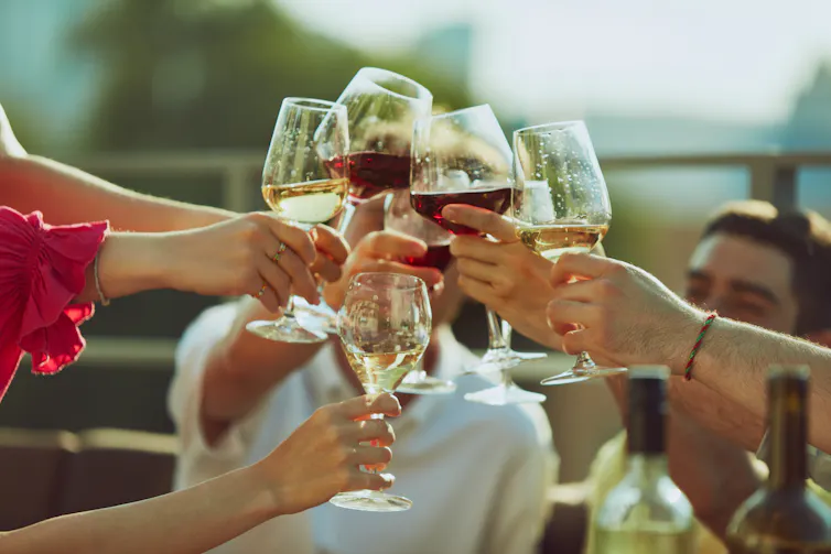 Many hands clinking full wine glasses together on a sunny evening.
