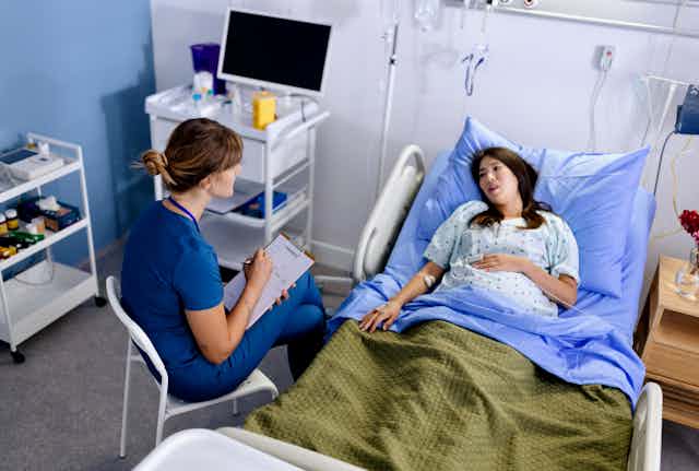 Female nurse taking notes and talking to a pregnant woman in a hospital bed.