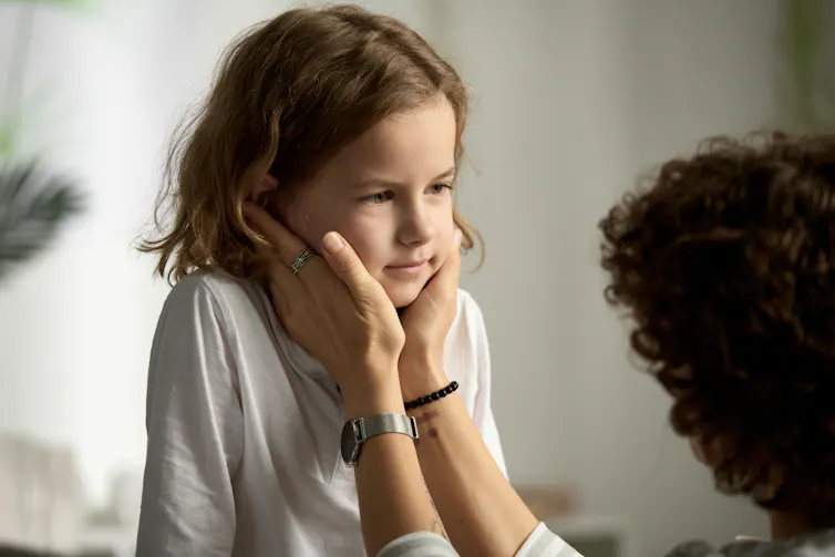 An adult gently puts their hands on a child's face.