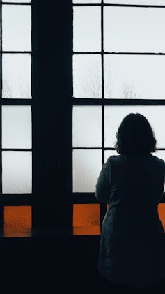 A woman with her back turned looks out of the window.