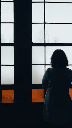 A woman with her back turned looks out of the window.