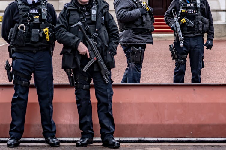 Photo of four armed police guarding a public space in London, shown from the neck down