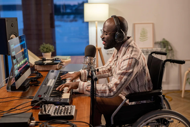 A young black man in a wheelchair recording some music at home with a computer and a piano keyboard.