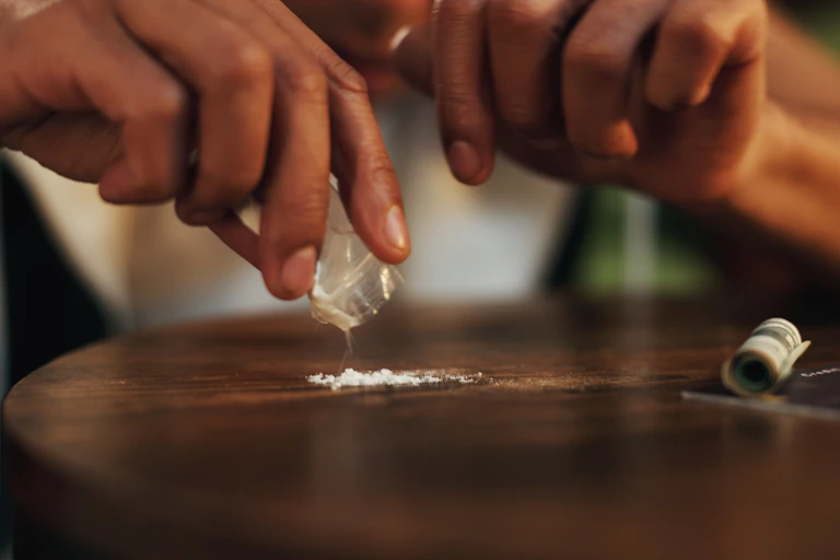A person pours cocaine from a plastic packet onto a table.