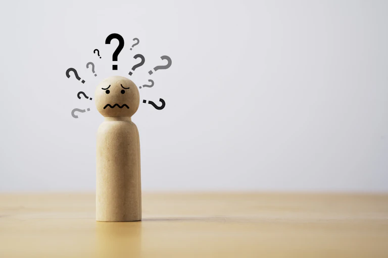 A wooden figure of a human with question marks around its head.