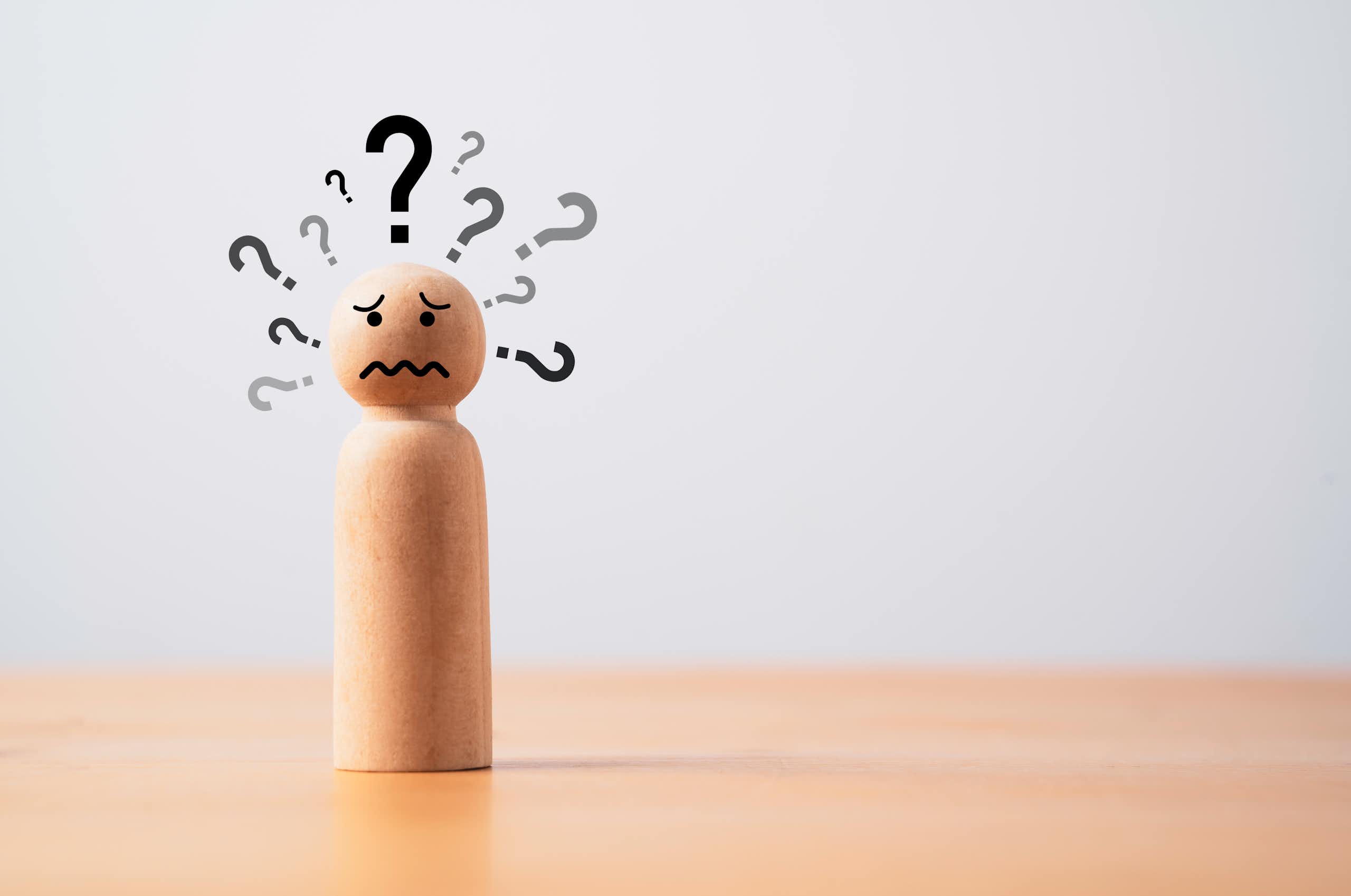 A wooden figure of a human with question marks around its head.