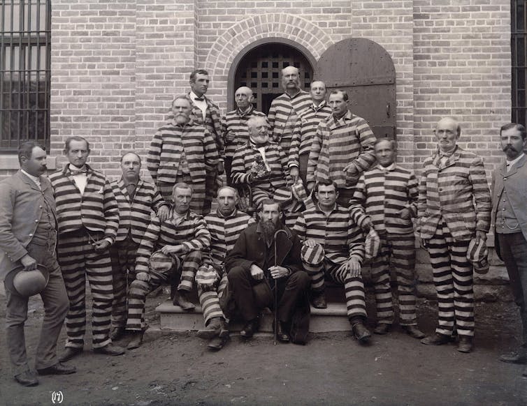 A black and white photo of two rows of men in striped uniforms posing outside a brick doorway.