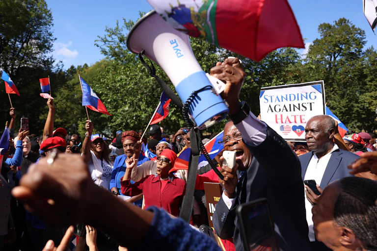 A Haitian pastor is surrounded by supporters as they demonstrate against hateful rhetoric aimed against them.