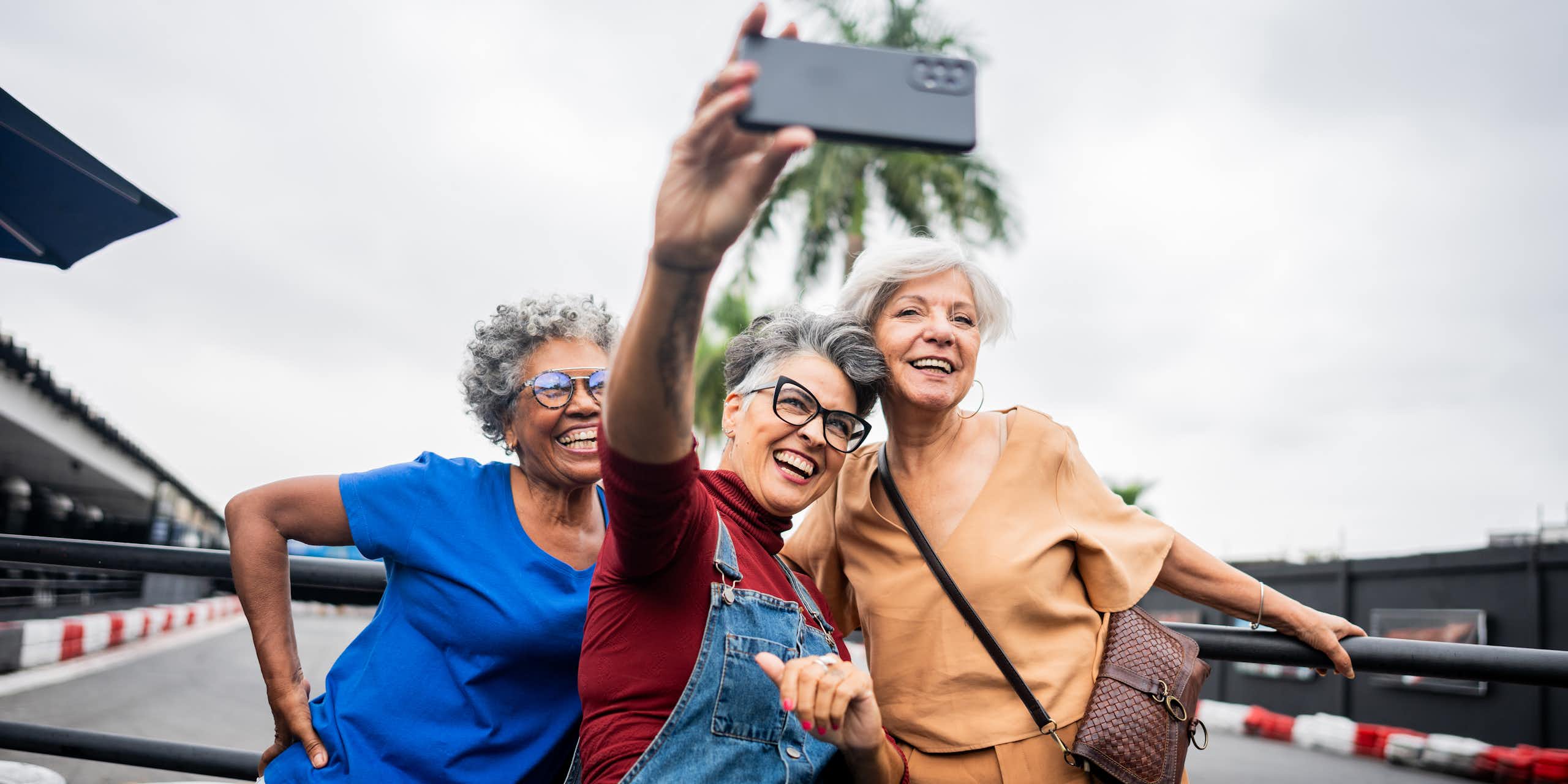 Three senior women smile as they look into their phone while taking a selfie