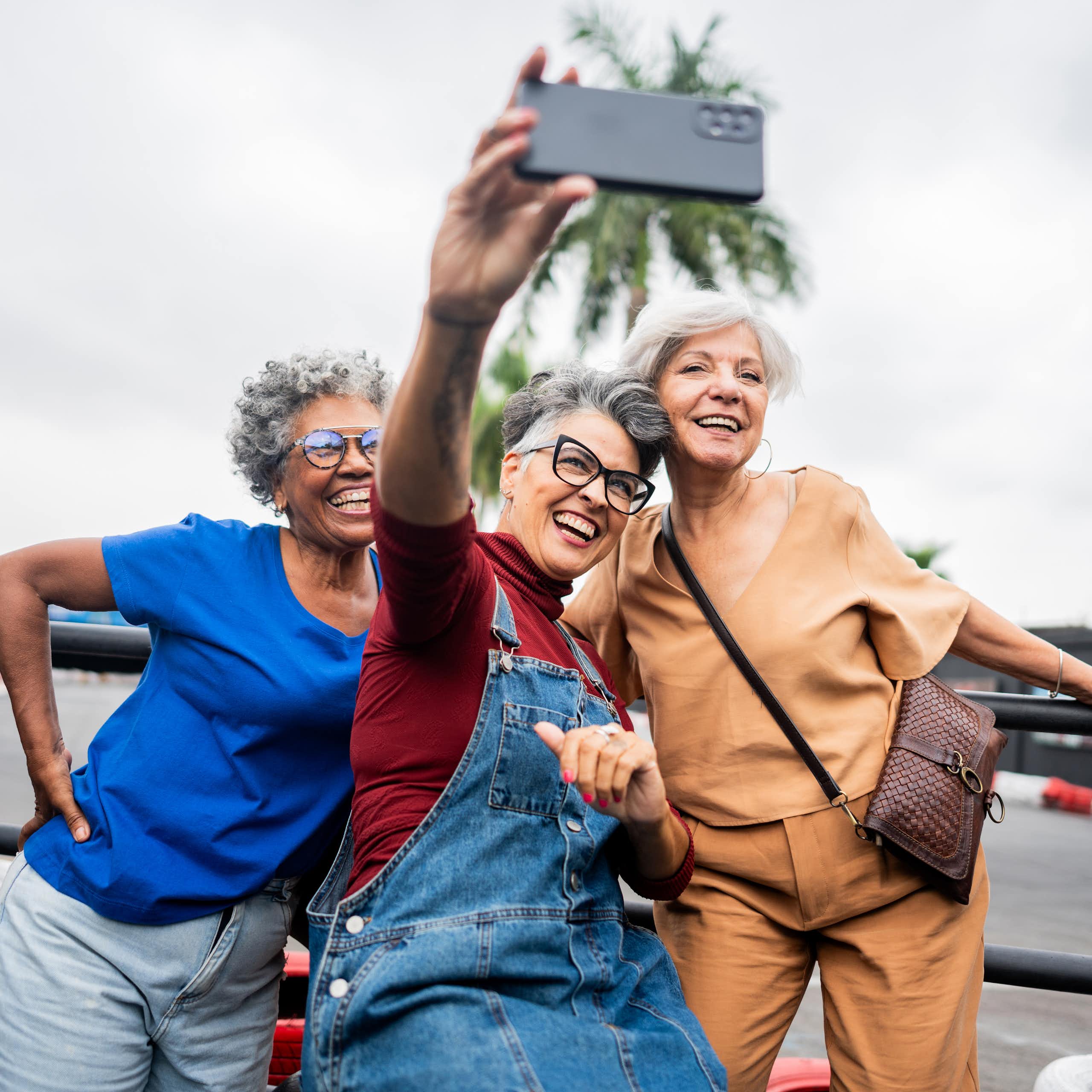 Three senior women smile as they look into their phone while taking a selfie
