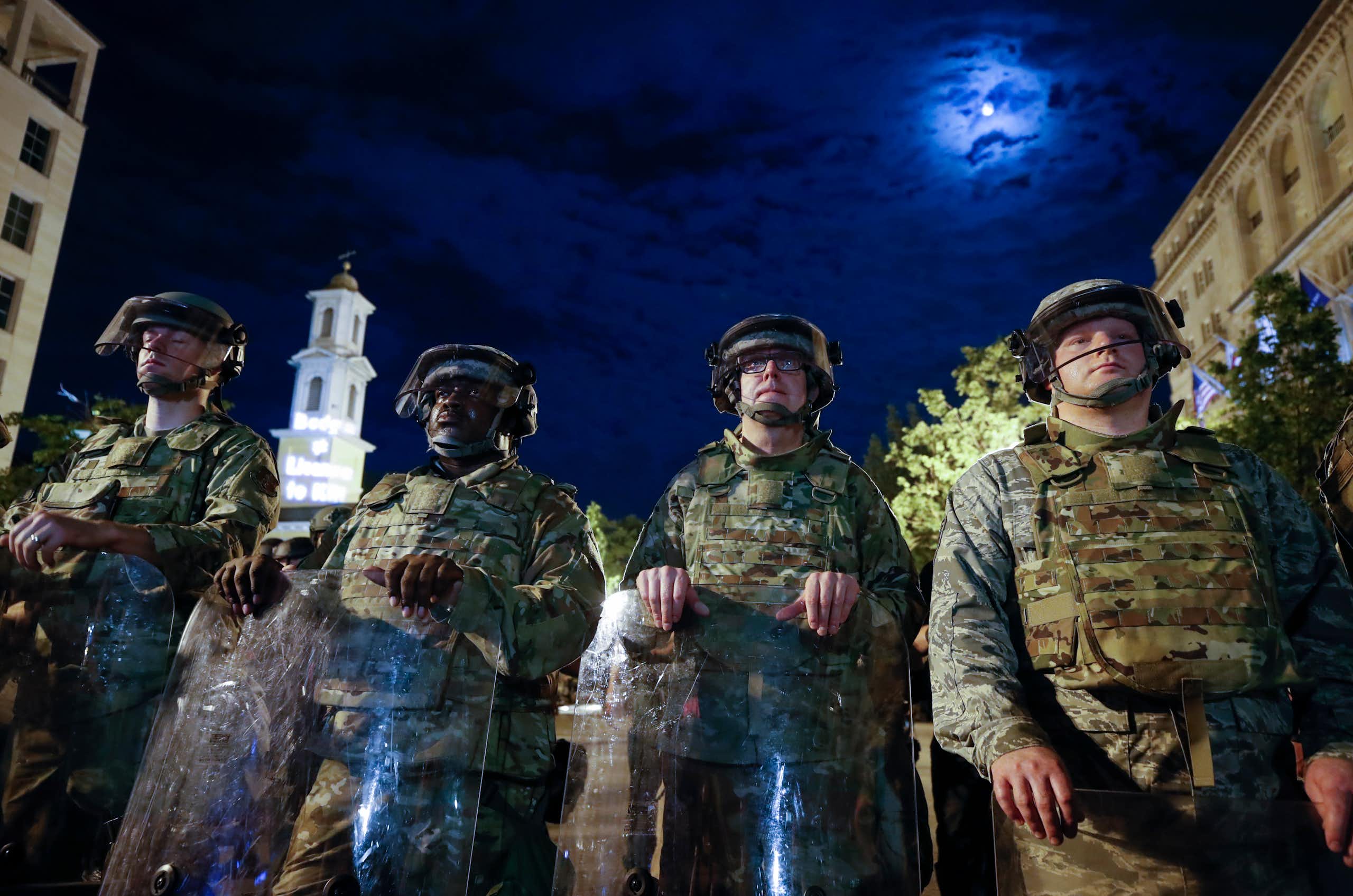 Men in helmets and camouflage uniforms stand in a row in a street.