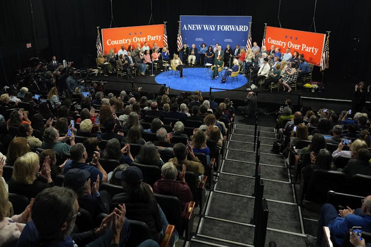 Three women sit on a stage with signs behind them that read Country Over Party and A New Way Forward.