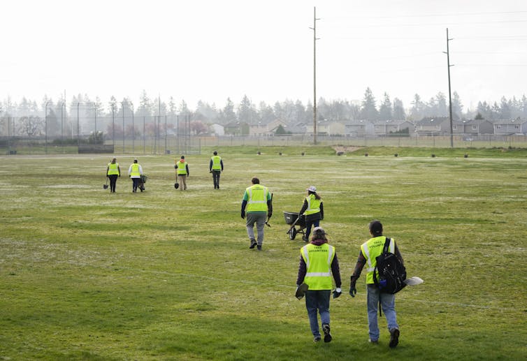 A group of people in bright green vests walk through an open field.