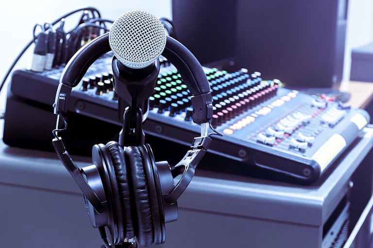 A set of headphones hangs on a microphone near a mixing board in a recording studio.