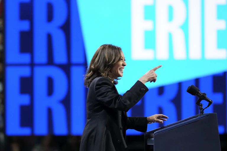 A dark-haired woman smiles as she speaks in front of large illuminted Erie logos