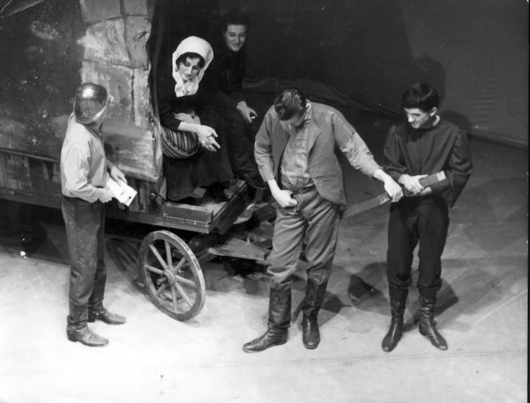 A woman sits on a wagon, three men stand.