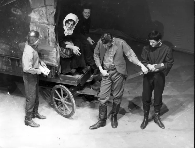 A woman sits on a wagon, three men stand.
