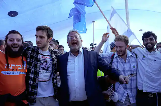 Israel's national security minister, Itamar Ben Gvir, dancing with members of the settler movement as Israeli flags fly in the background.