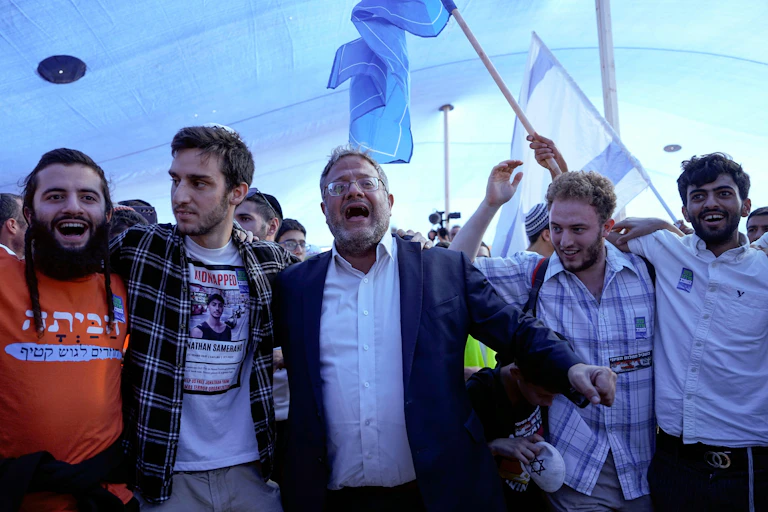 Israel's national security minister, Itamar Ben Gvir, dancing with members of the settler movement as Israeli flags fly in the background.