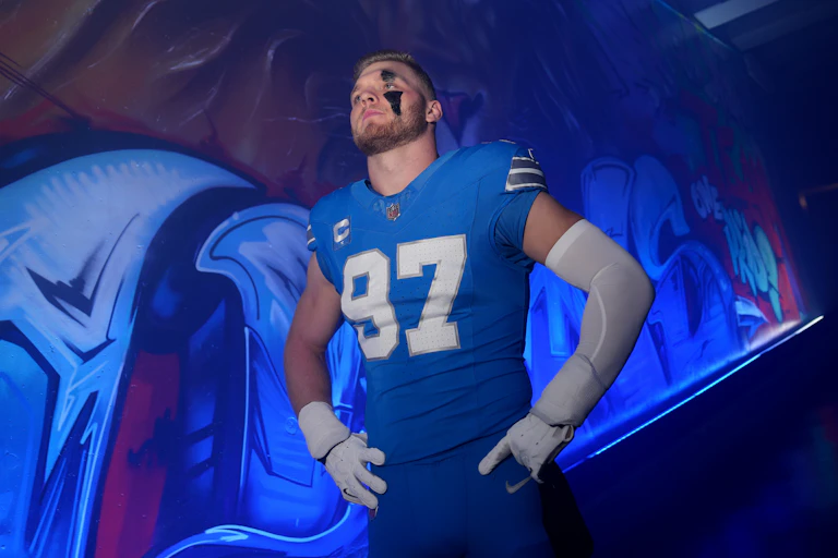 Football player wearing blue No. 97 jersey and black paint above and below left eye stands with hands on hips