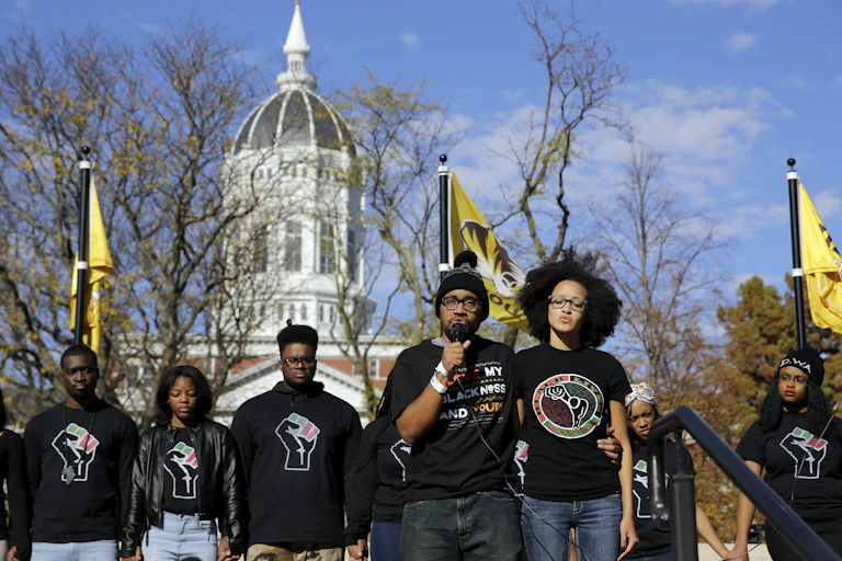 Black students speak in front of a campus building wearing black shirts