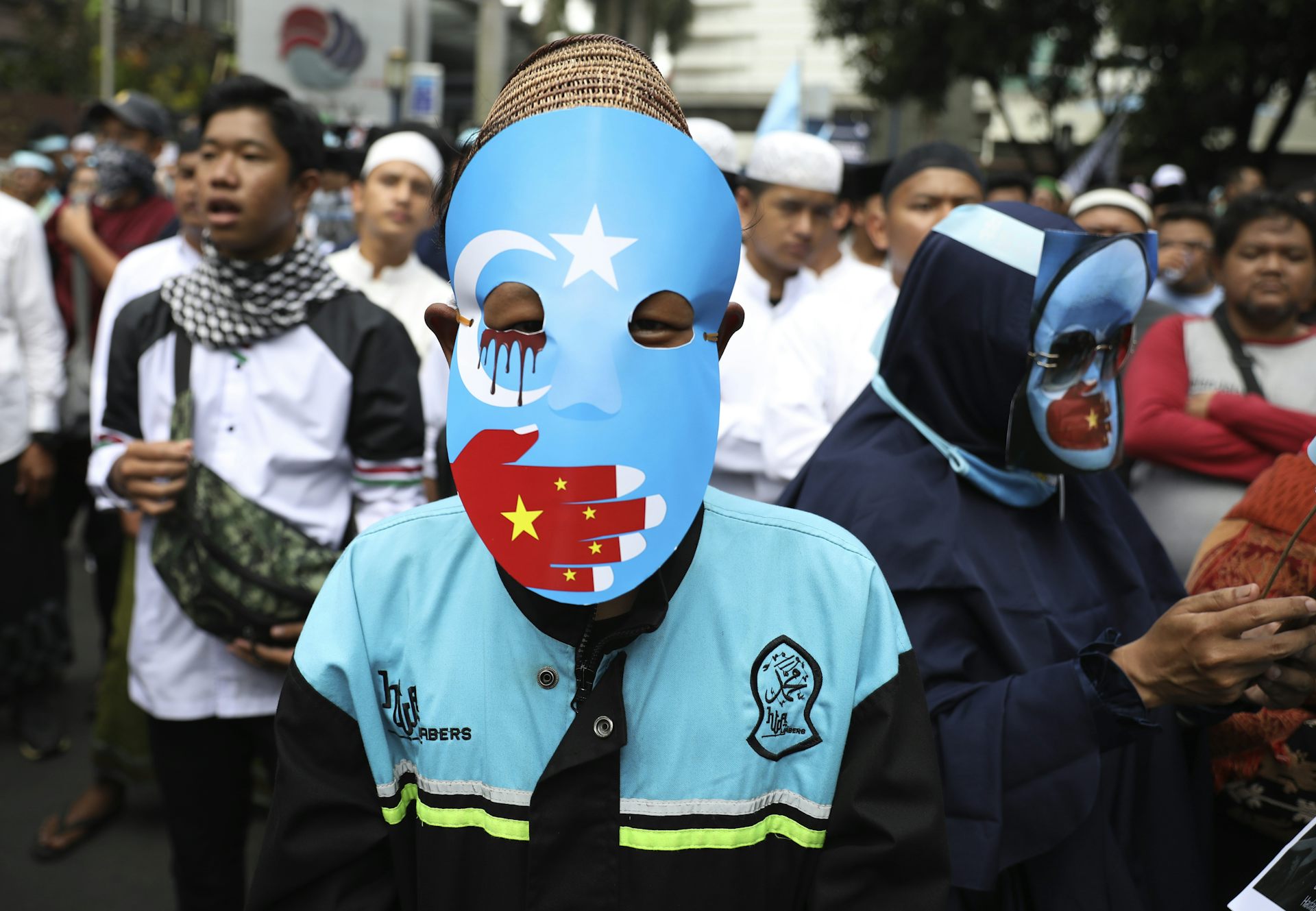 A protestor in a blue mask with a red hand over the mouth.